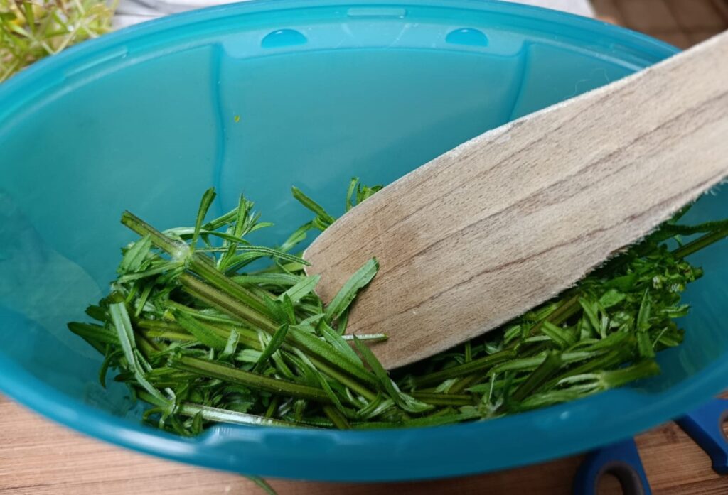 Kleefkruid met een houten lepel kneuzen om er daarna een detox drankje van te maken