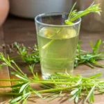 Een glas vers kleefkruid extract op een houten tafel met verse Galium aparine takjes in het zonlicht.