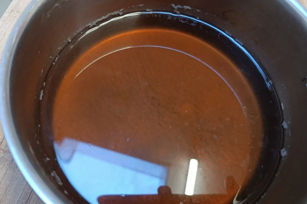Een helder, gezeefd donkerbruin kruidenextract in een pan, de basis voor de krachtige slijmoplossende hoestsiroop.