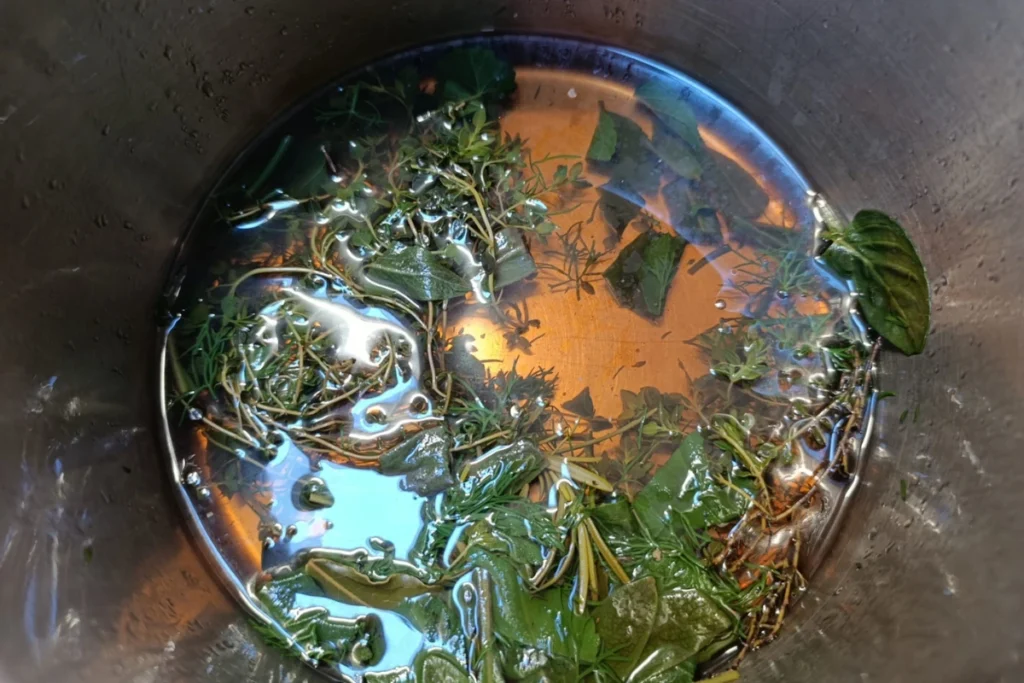 Het resultaat van de kruideninfusie in de pan na het trekken, waarbij de vloeistof een diepe, goudbruine kleur heeft gekregen.