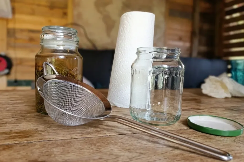 Schone glazen bokaal met een metalen zeef en keukenrol op een houten tafel ter voorbereiding van het maken van een dennentinctuur.