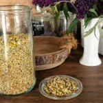 Zelf Kamille Drogen: Een grote weckpot met gedroogde kamille bloemen en een schotelje ernaast met gedroogde bloemen erop, op een mooie houten tafel
